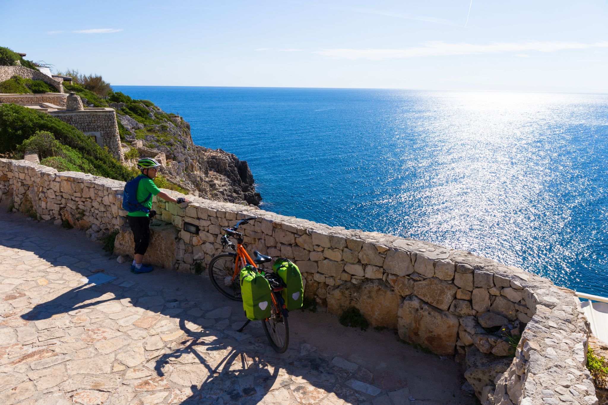 Cicloturista, borse da bici, muretto, scogliera frastagliata, mare cristallino, slow tourism, Puglia